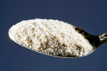 Closeup of ground Indian flea seeds on a spoon isolated on dark blue background