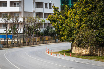 A car road bends around a bend along a city street, with white houses, sidewalks, green trees on a warm summer day