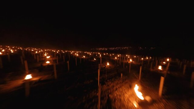 Slow frontwards aerial of Candles burning to heat up the Vineyards in Chablis, France at night. DJI FPV
