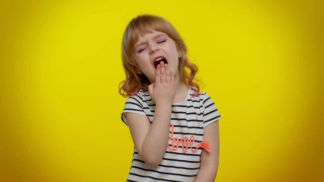 Tired little blonde teen kid child girl yawning, sleepy inattentive feeling somnolent lazy bored gaping suffering from lack of sleep on yellow studio background. Young children lifestyle emotions