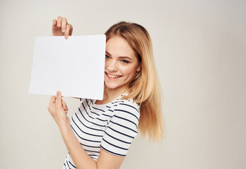 Naklejka premium Woman in striped T-shirt blonde hair and a white sheet of paper on a beige background