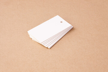 stack of white blank rectangular paper tag labels for clothing price tags on beige brown cardboard background, isolated.
