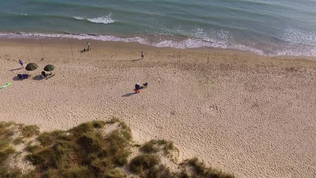 Beautiful coast line with vegetation on one side and the seas hore on the other. A few fisherman are seen with the lines set and also some walkers seen along the beach.