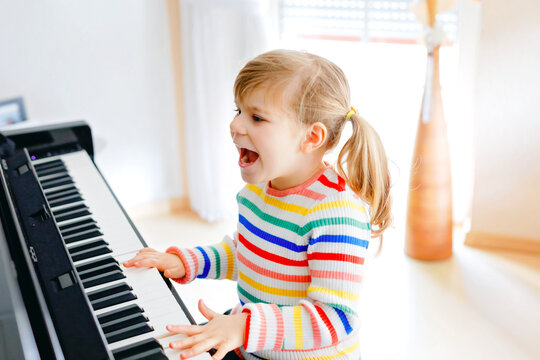 Beautiful little toddler girl playing piano in living room. Cute preschool child having fun with learning to play music instrument with learning concept during homeschooling corona virus lockdown.