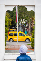 Travel concept. A little boy looks through a white doorway, a window at a yellow taxi moving across...