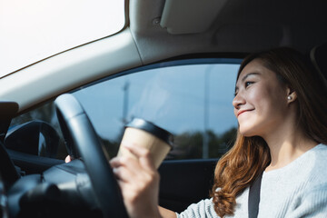 A young asian woman holding and drinking coffee while driving a car