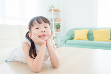 Little asian girl sitting alone in living room and looking at camera with boring face.