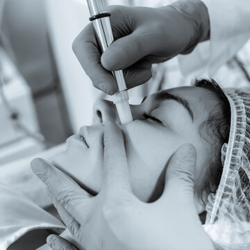 Cosmetologist doing microdermabrasion procedure for woman to refresh her skin tone. black and white image with blue tint to emphasize the concept of high technology