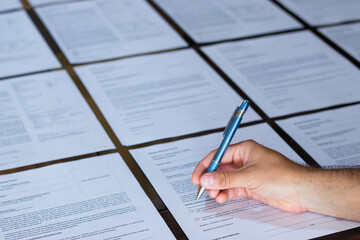 Hand of a young adult man signing a stack of contract or agreement papers with a metallic blue pen