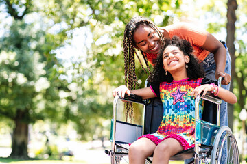 Little girl in a wheelchair at the park with her mother.