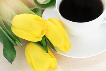 A bouquet of yellow tulips near a white saucer with a cup of coffee. Postcard. Wallpaper