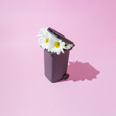A creative nature concept with white flowers growing from a trash can against a pastel pink background. Minimal spring and nature concept