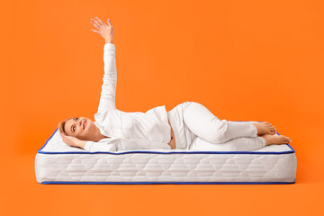 Mature woman lying on soft mattress against color background