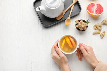 Woman holding cup of tasty ginger tea on light wooden background