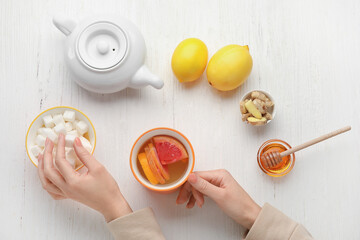 Female hands with cup of tasty ginger tea and sugar on light wooden background