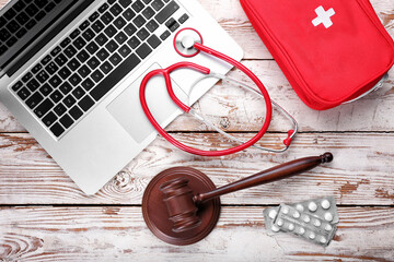 Judge gavel, pills, laptop, first aid kit and stethoscope on wooden background. Concept of health...