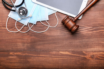 Judge gavel, tablet computer, masks and stethoscope on wooden background. Concept of health care reform