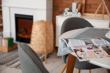 Magazine on table in interior of modern dining room with fireplace, closeup