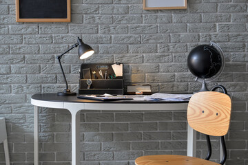 Modern workplace with glowing lamp near brick wall