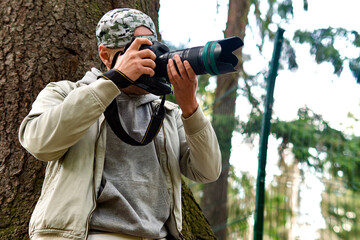 Photographer in white photographs nature with a telephoto lens leaning on a tree