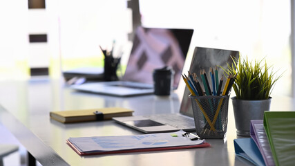 Meeting table with computer laptop, house plant, pencil holder, office supplies and document.