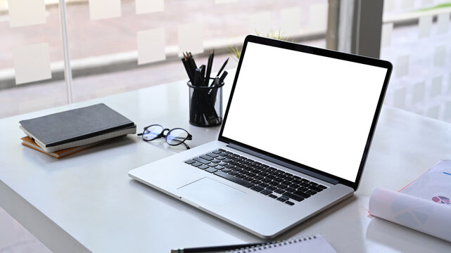 Modern workspace with computer laptop, pencil holder, document, glasses and notebook on white desk.