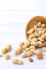 Peanuts with leaf in wooden basket and peanuts in the peel scattered isolated on wooden white background.Healthy vegetarian concept.