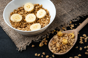 Granola with banana in white bowl on black background.