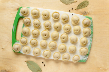 Raw russian dumplings with bay leaf and pepper on wooden table, top view