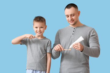 Father and little son brushing teeth on color background