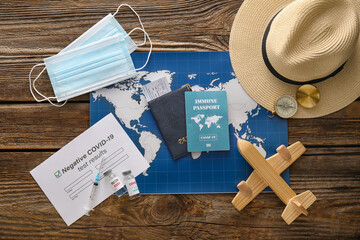 Travel supplies, covid-19 test result and immune passport on wooden background