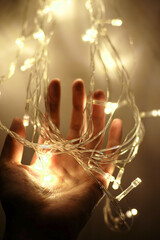White Christmas lights on an open palm of the hand, Hand holding white/yellow Christmas lights, Long string of Christmas lights on a hand