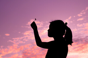 Little girl making a wish under the night sky, Shadow of a child holding a white grass flower under purple sky