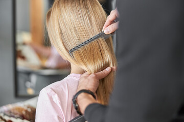 Pofessional hairdresser is combing a hair of beautiful caucasian blonde woman in modern salon