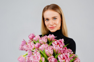 Portrait of a beautiful young woman in dark with pink tulips on a gray background, floristics