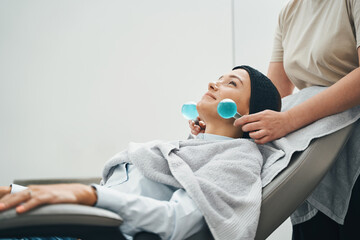 Dermatologist massaging the female patient face with two ice globes - obrazy, fototapety, plakaty