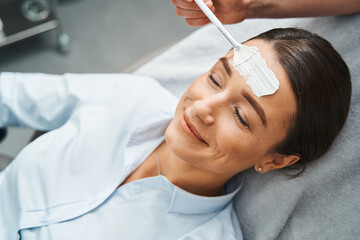 Naklejka premium Cosmetician applying a skincare product on the patient forehead