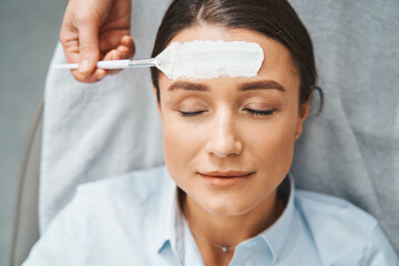 Cosmetician hand applying a skincare product on the woman forehead