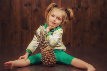 Beautiful and cute baby girl sitting on the floor in her hands a pineapple