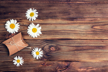 Festive background with daisies and a gift on wooden planks.