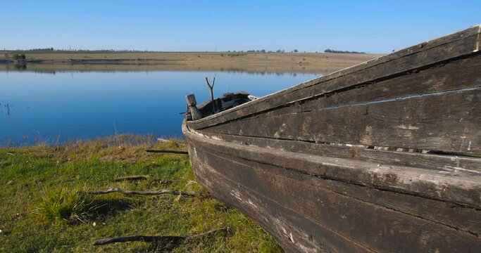 Tracking  shot of the bow of an old wooden boat abandoned on the shore of a lake on a sunny day. 4k 50 fps

