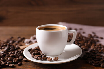 Cup of hot aromatic coffee and roasted beans on wooden table, closeup