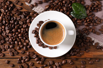 Cup of hot aromatic coffee and roasted beans on wooden table, flat lay