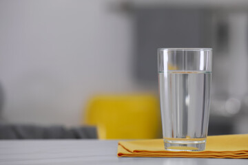 Glass of water and napkin on white table against blurred background. Space for text