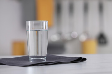 Glass of water and napkin on white table against blurred background. Space for text