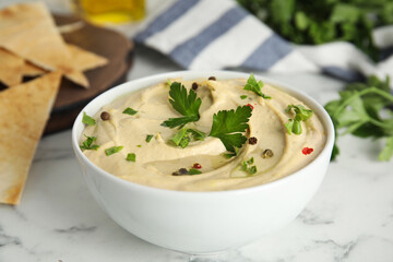Delicious hummus with parsley and pita chips on white marble table, closeup