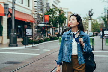 Fototapeta premium woman backpacker with sunglasses on head is appreciating the beauty of the small town. female commuter is looking at surroundings along the street on her way to school.