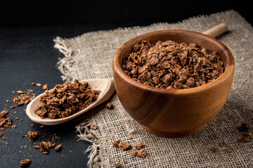 Chocolate granola in wooden bowl on black background.