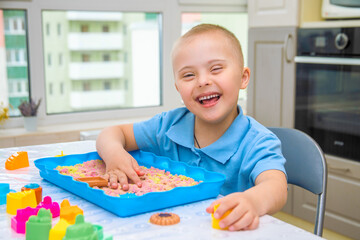 Portrait of a cute boy with Down syndrome, a child playing with sand and molds for modeling, early development, children andwalids.
