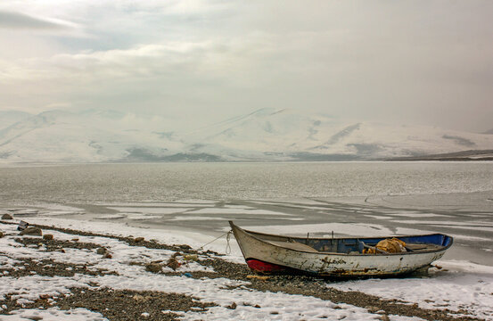A worn-out old fishing boat tied up on the beach on a frozen lake in winter, &Ccedil;ıldır Lake, Kars, Turkey.
